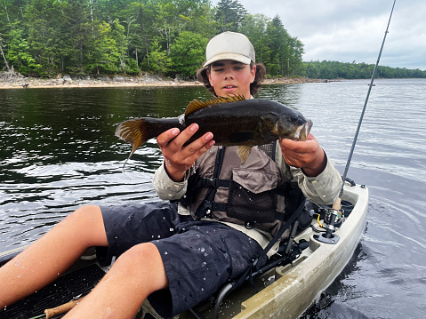 A happy fisherman with a nice smallmouth bass caught kayak fishing on a lake