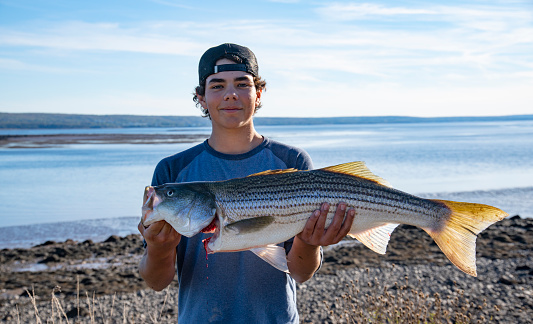 A teen fisherman with a freshly caught striped bass from the sea