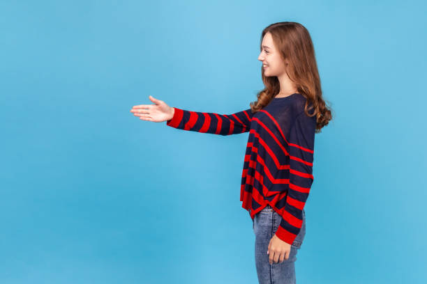 Nice to meet you! Side view portrait of young beautiful woman wearing striped casual style sweater giving hand to handshake and smiling. stock photo
