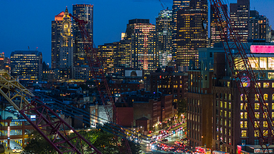 Construction cranes in front of the illuminated night city skyline of Boston, Massachusetts.