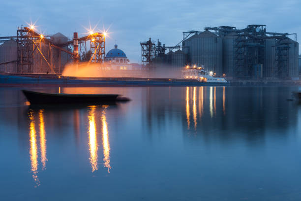 Night loading process of cargo barges with wheat grain for export at the river port at night on long exposure. An urban landscape stock photo