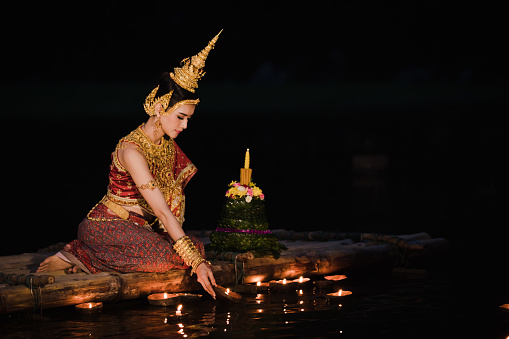 night portrait model wearing traditional thai red and purple and gold jewelry on loy krathong day in the water park to soft fucus blur and noise