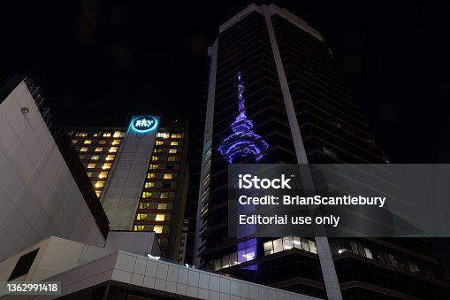istock Night scene tall circular tower illuminated blue reflected in glass facade of surrounding building. 1362991418