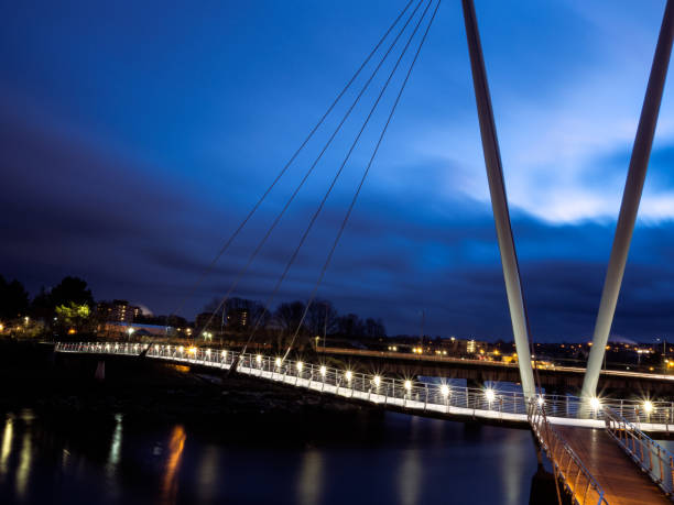 NIght view of Footbridge in Lancaster UK Night view of Millenium bridge in Lancaster over River Lune with dark blue stormy sky, bright lights and reflections Lancaster, Lancashire stock pictures, royalty-free photos & images