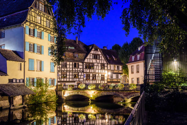 Night view of the river Ill canal in the Petite France quarter in Strasbourg, France. Night view of the Pont du Faisan spanning the river Ill canal in the Petite France quarter in Strasbourg, France, lined with half-timbered buildings reflecting in the still waters. historic district stock pictures, royalty-free photos & images