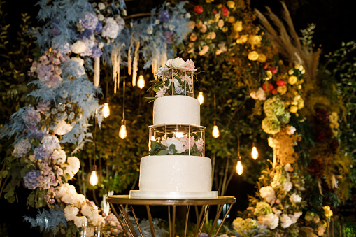 Night wedding ceremony, the arch is decorated with flowers, candles and garlands and there is a wedding cake on the table