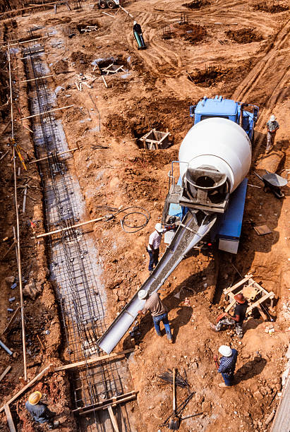Nineteen Nineties Era Construction Site Construction workers pour cement footing for a commercial building. There are several workers scattered around the construction site in this image which was made in 1991. 1991 stock pictures, royalty-free photos & images
