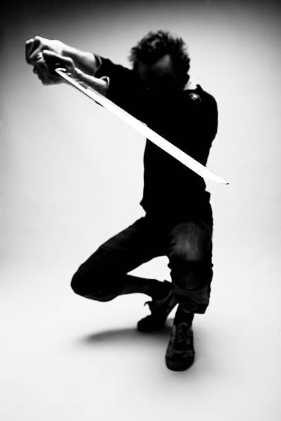 Ninja Contemporary ninja in the shadows posing with sword. Very shallow depth of field with focus on the blade. Canon 1Ds Mark 2 file bruce springsteen stock pictures, royalty-free photos & images