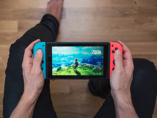 Nintendo Switch neon Game Console Gothenburg, Sweden - March 10, 2017: A shot from above of a young man's hands holding a neon coloured Nintendo Switch video game system developed and released by Nintendo Co., Ltd. in 2017. The system is turned on and the game The Legend of Zelda, Breath of the Wild is showing on the display. Shot on a hardwood floor background in a home environment. switch stock pictures, royalty-free photos & images