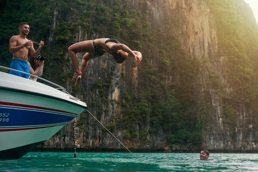 Shot of a young woman doing a backflip off a boat while her friends watch