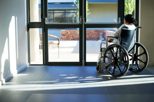 An old woman sitting in a wheelchair at the the door of an institution