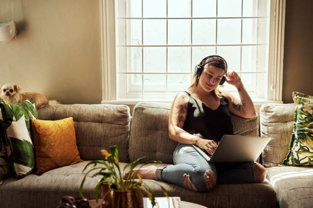 No words needed, just music Shot of a young woman using a laptop and headphones on the sofa at home voluptuous women images stock pictures, royalty-free photos & images