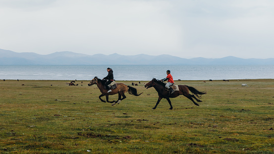 August 27th, 2020 - Woman and a young man having fun playing an old game riding horses in the nomad village by the big lake in Kyrgyzstan
