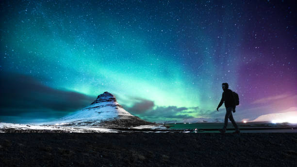 Northern lights in Mount Kirkjufell Iceland with a man passing by Solo traveler walking in front of an awesome Northern Lights in Mount Kirkjufell Iceland. astronomy photos stock pictures, royalty-free photos & images
