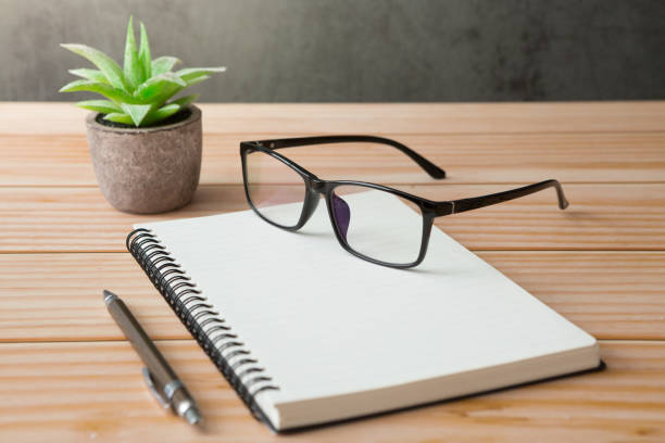 Notebooks, pens, glasses, cactus on wooden desks and loft walls with sunlight and copy space stock photo