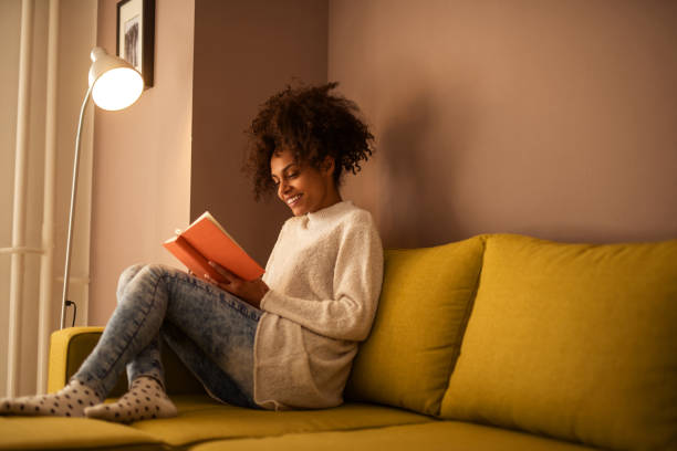 Nothing beats a good book Portrait of a beautiful african american smiling woman reading a book at home. reading stock pictures, royalty-free photos & images