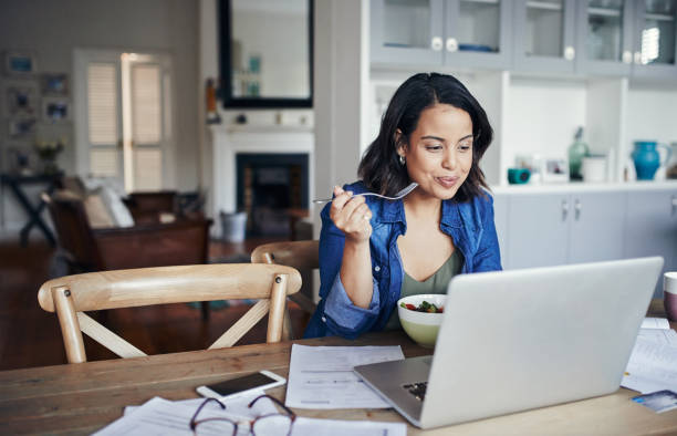Nothing inspires productivity like a healthy lunch Shot of a young woman using a laptop and having a salad while working from home lunch stock pictures, royalty-free photos & images