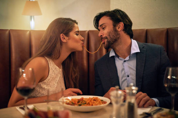 Nothing inspires romance quite like Italian food Shot of a young couple sharing spaghetti during a romantic dinner at a restaurant spaghetti stock pictures, royalty-free photos & images