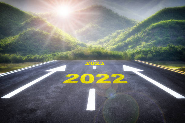 Number of 2022 to 2023 on asphalt road surface with arrow sign on the mountain background stock photo