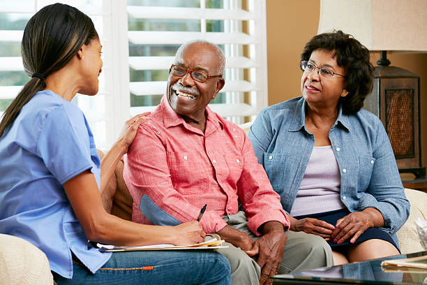 Nurse and senior couple talking at a home visit Nurse Making Notes During Home Visit With Senior Couple Smiling home caregiver stock pictures, royalty-free photos & images