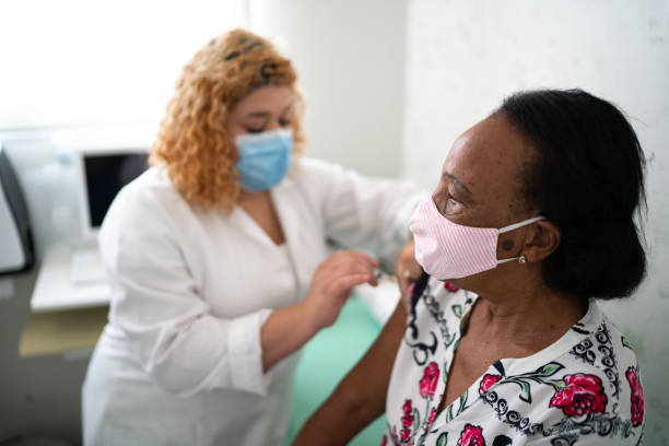 krankenschwester, die mit gesichtsmaske einen impfstoff auf den arm des patienten aufträgt - impfung stock-fotos und bilder