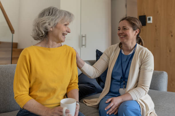 A nurse conducts an interview with a patient at home in a happy mood over coffee. stock photo