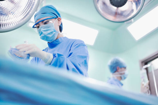 Nurse holding anesthesia mask in operating room Female Asian Chinese woman nurse OR staff surgeon holding surgical anesthesia mask tube dressed in safety gown scrubs and performing operation in operating room medical facility hospital healthcare anesthetic stock pictures, royalty-free photos & images