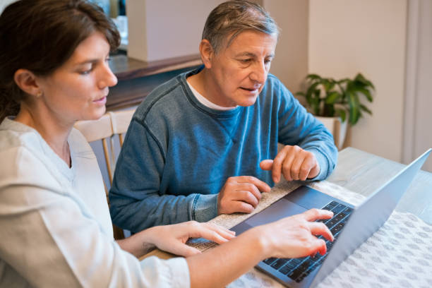 Nurse teaching laptop to senior man at home Caregiver teaching laptop to senior man. Elderly male is learning wireless technology. They are at home. social work online stock pictures, royalty-free photos & images