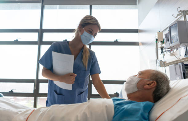 Nurse wearing a facemask while checking on a patient at the hospital Nurse wearing a facemask while checking on a patient at the hospital during the COVID-19 pandemic hospital ward photos stock pictures, royalty-free photos & images