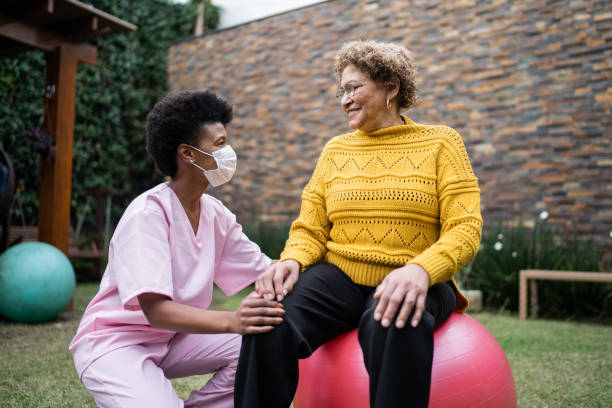Nurse with senior patient doing exercise at home - using protective face mask Nurse with senior patient doing exercise at home - using protective face mask yoga ball work stock pictures, royalty-free photos & images