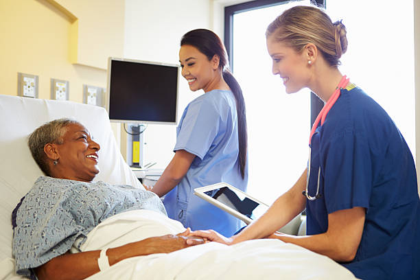 Nurse with tablet talking to senior woman Smiling Nurse With Digital Tablet Talks To Female Patient In Hospital Bed hospital ward photos stock pictures, royalty-free photos & images