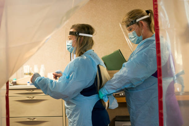 Nurses don PPE to enter quarantined rooms Two blond nurses don PPE protective gear of plastic gowns, face masks, face shields and gloves prior to entering a quarantined patient's room in isolation during the Covid-19 pandemic, Midwest, USA inpatient stock pictures, royalty-free photos & images