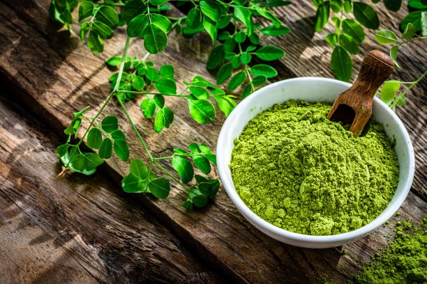 Nutritional supplement: Moringa powder on rustic table Nutritional supplement: high angle view of Moringa oleifera powder in a white bowl shot on rustic wooden table. Green Moringa leaves are around the bowl. High resolution 42Mp studio digital capture taken with Sony A7rII and Sony FE 90mm f2.8 macro G OSS lens moringa stock pictures, royalty-free photos & images