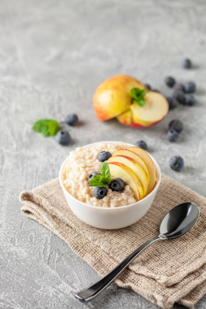 Oatmeal porridge bowl with blueberry, apples and mint leaves. Healthy breakfast stock photo