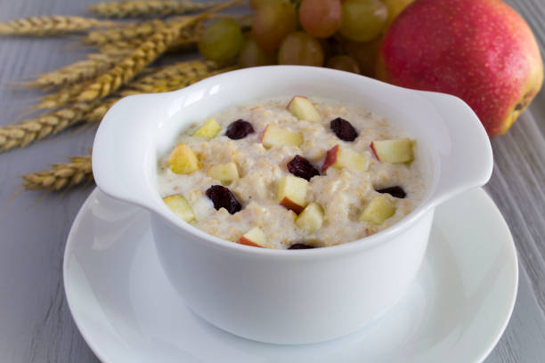 Oatmeal with milk, apple and raisins in the wtite bowl on the gray wooden background. Close-up. stock photo