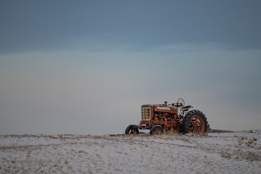 Obsolete and retired antique farm tractor on a snow covered hill in central Montana in western United States of America (USA). Light snow falling and foggy.