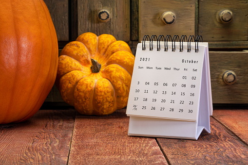 October 2021 - spiral desktop calendar on a weathered barn wood table with rustic apothecary drawers, pumpkin and squash in background, time and business concept