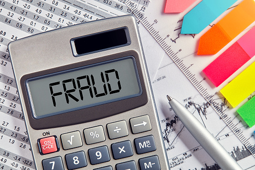 Office desktop with calculator displaying the word fraud. Business and financial crime concept.