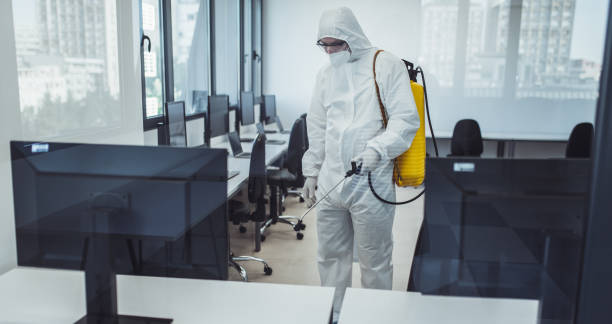 Office disinfection during COVID-19 pandemic. Man in protective suit and face mask spraying for disinfection in the office stock photo
