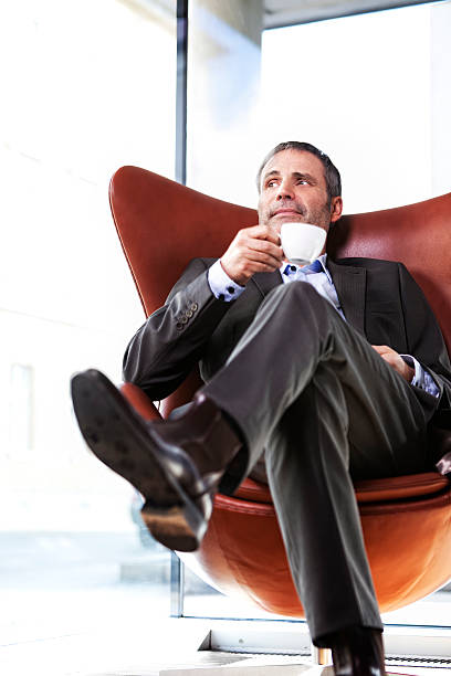 Smiling senior businessman in grey suit sitting in red office chair...