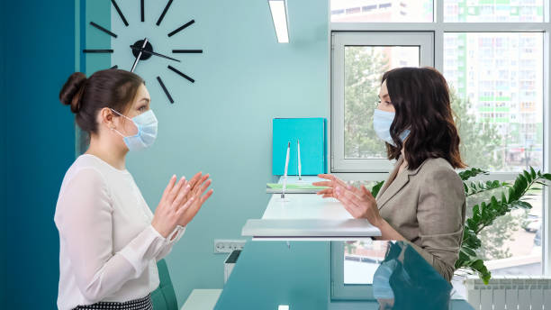 Office manager with mask talks to lady patient near counter stock photo