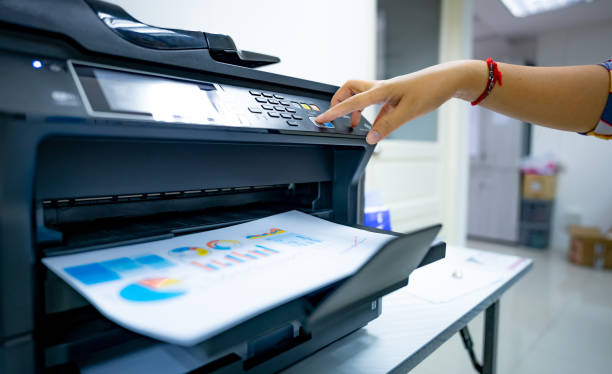 Office worker prints paper on multifunction laser printer. Copy, print, scan, and fax machine in office. Document and paper work. Print technology. Hand press on photocopy machine. Scanner equipment. stock photo