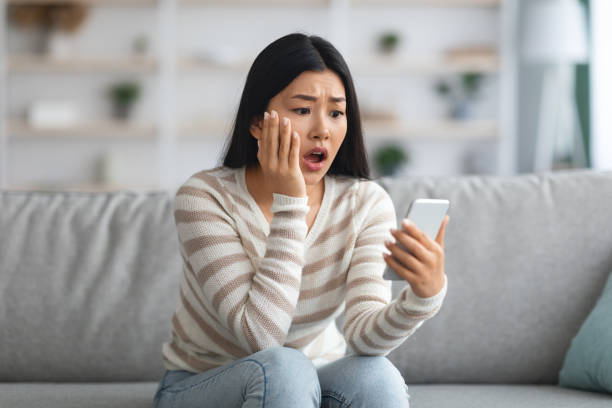 oh no. shocked asian woman reading bad message on smartphone at home - bedrägeri telefon bildbanksfoton och bilder