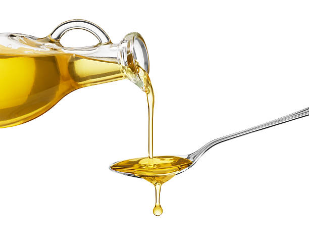 Oil being poured from a large bottle onto a spoon pouring oil on spoon from glass bottle cooking oil stock pictures, royalty-free photos & images
