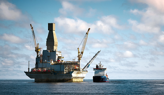 Oil rig offshore drilling platform and support vessel. Blue cloudy clear sky, sea surface