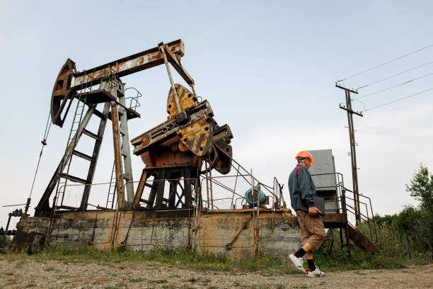 Oil worker engineer walking in front of oil pumpjack Oil worker engineer walking in front of oil pumpjack oil stock pictures, royalty-free photos & images