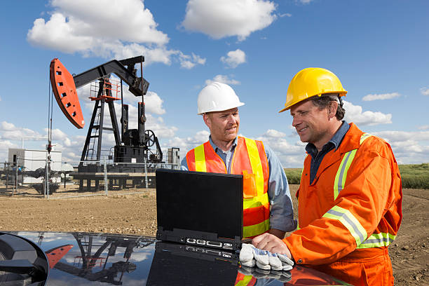 Oil Workers and Laptop A royalty free image from the oil industry of two oil workers using a laptop in front of a pumpjack oil and gas industry stock pictures, royalty-free photos & images