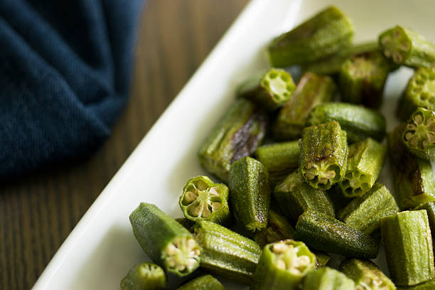 okra roasted on white platter Roasted okra pieces on a white platter with a blue napkin behind it.  Selective focus. okra photos stock pictures, royalty-free photos & images