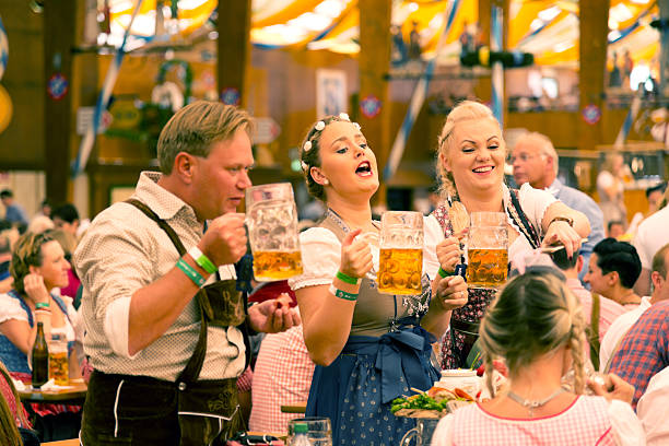 Munich, Germany - September 29, 2016: Oktoberfest in Munich, Germany. A group of young people in beer hall, celebrating Oktoberfest on Theresienwiese. People are dressed in traditional clothes and holding beer glass. The Oktoberfest is the largest fair in the world and is held annually in Munich.