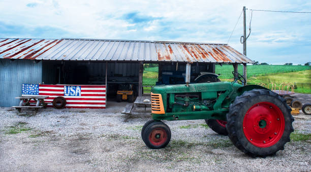 Old antique farm tractor parked in front of shed and hand painted American flag stock photo